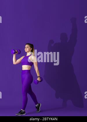 Superhero in shadow of ordinary people - modern superhero's concept, respect and admiration. Young woman stays active, sportive setting good example. Inspiring others to be strong and healthy. Stock Photo