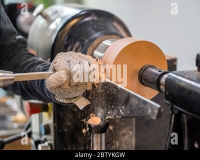 Carpenter man is shaving surface of the wooden bowl. Spinning wood wheel. Carving outside forming a round detail. Joiner is using metal tool to make t Stock Photo