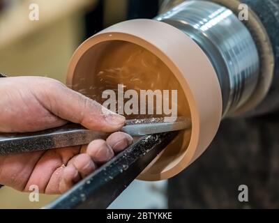 Carpenter man is shaving the wooden bowl. Spinning wood wheel. Carving inside forming a round detail. Joiner is using metal tool to make the handmade Stock Photo