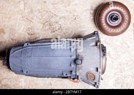Separately, the car parts on the fiberboard sheet are an automatic metallic blue gearbox with a brown torque converter in the workshop for repair or f Stock Photo