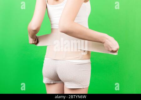 Back view of pregnant woman putting on supporting bandage to