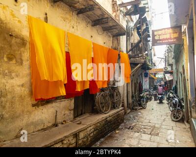 Varanasi, Uttar Pradesh, India - February 2015: Saffron dyed clothes hanging outside an old house in a narrow cobbled alley in the old city. Stock Photo
