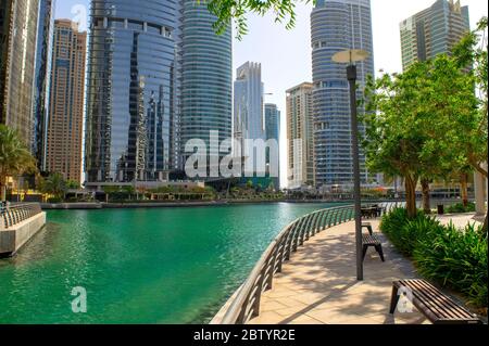 Dubai / UAE - May 26, 2020: View of Jumeirah Lakes Towers skyscrapers with an artificial lake. Beautifully tiled pavement with benches among the lake in JL Stock Photo