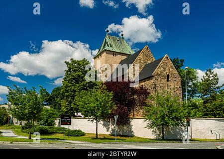 Kyje, Prague / Czech Republic - May 27 2020: View of the Church of Saint Bartholomew made of stone standing behind a wall. Green trees, sunny day. Stock Photo