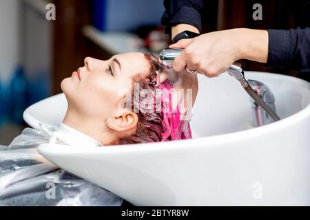 Side view of hands of hairdresser washing off the paint with hair of woman in white sink in hair salon. Stock Photo