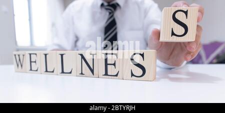 The word wellness from wooden cubes. Man in shirt and tie on the background. Close up. Stock Photo