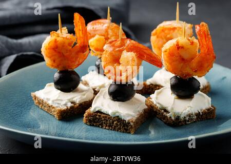 Canapes with grilled shrimps, olive, cream cheese and bread. Party food. Stock Photo