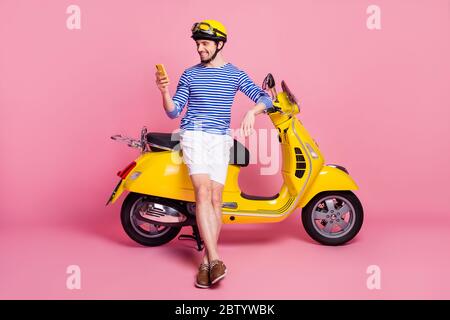 Portrait of his he nice attractive handsome cheerful cheery focused guy sitting on moped using cell app 5g taxi service order isolated over pink Stock Photo
