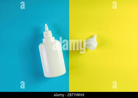 White plastic bottle and cap on blue and yellow background. Aerosol from common cold or allergy, spray for nose, medical drops. Top view, copy space Stock Photo