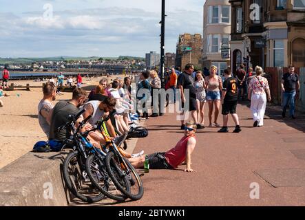 Portobello, Scotland, UK. 28 May 2020. Warm sunny weather with temperatures reaching 24C brought many people to the beach and promenade at Portobello, Edinburgh. The public seem to sense that the lockdown is being relaxed are are taking advantage of the good weather to sunbathe and enjoy the many cafes that are now offering takeaway snacks. Iain Masterton/Alamy Live News Stock Photo