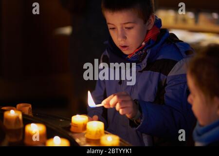 child with a match is going to light a candle inside a church Stock Photo