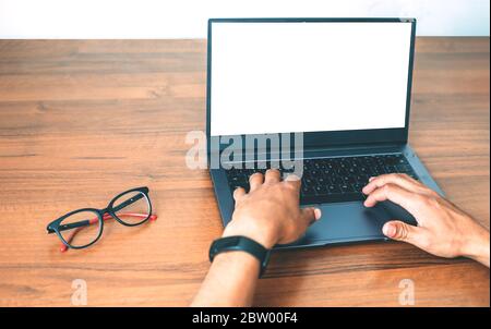 Men's hands in black electronic watches on the keyboard of a laptop with a white isolated screen against the background of a wooden table Stock Photo