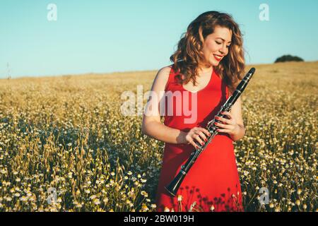 woman in a red dress in the field playing the clarinet Stock Photo