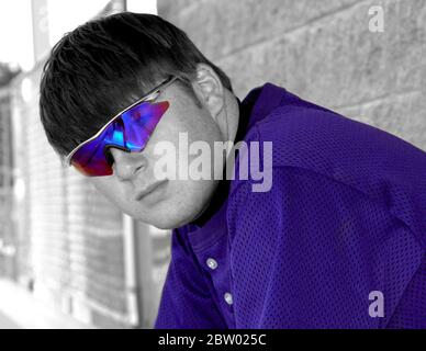 High school baseball player is wearing his purple uniform with his favorite accent, purple sunglasses.  Image is black and white with purple color. Stock Photo