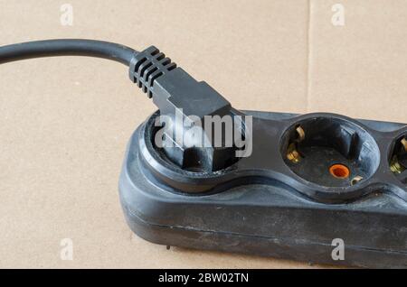 Used electric extension cord on a beige background. Black developer with a plug in the plug. Electrical Safety Rules. Close-up. Selective focus. Stock Photo