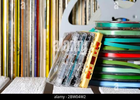 Stacked magnetic tapes and vinyl records on the shelf are visible in a background. Stock Photo