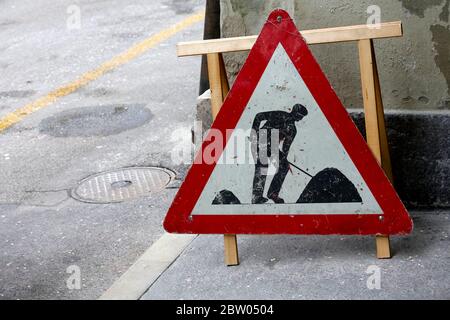 Road works sign is placed somewhere next to the street and it is visible just by the building wall. Stock Photo