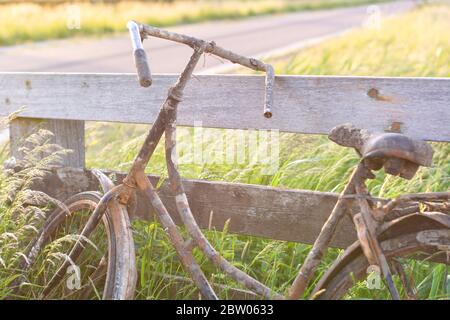 An old abandoned rusty bike parked against a wooden fence. Old fashioned classic bicycle stands forgotten along a bicycle path. Stock Photo