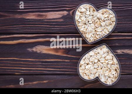 Muesli in bowl heart shaped on dark natural wooden board background. Raw oatmeal. Empty place, copy space for text Stock Photo