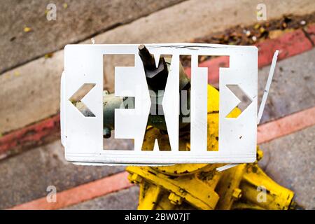 White Exit sign stuck on fire hydrant on sidewalk.  Abstract image of broken Exit sign in color horizontal photograph. Stock Photo