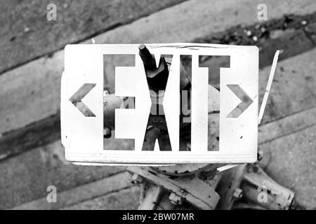 White Exit sign stuck on fire hydrant on sidewalk.  Abstract image of broken Exit sign in black & white horizontal photograph. Stock Photo