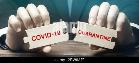 A man collects wooden puzzles with the words Covid-19 and Quarantine. Coronavirus pandemic infection COVID-19. Isolation of people. Obstruction of the Stock Photo