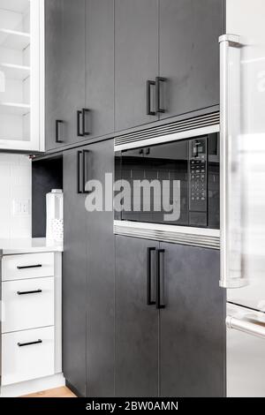 A detail shot of some dark grey / black cabinets in a modern condo with a Wolf microwave built in and a Sub-Zero refrigerator to the right. Stock Photo