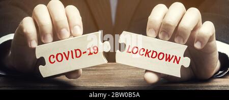 A man collects wooden puzzles with the words Covid-19 and Lockdown. Coronavirus pandemic infection COVID-19. Isolation of people. Obstruction of the s Stock Photo