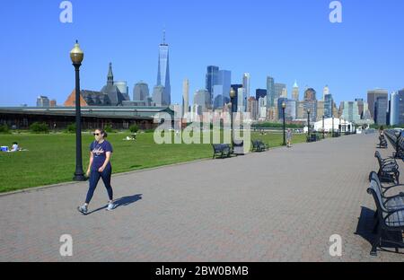 A young woman wearing mask walking at empty Hudson river waterfront walkway in Liberty State Park during covid-19 pandemic outbreaking with Lower Manhattan skyline in the background.Jersey City.New Jersey.USA