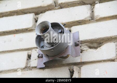 An old rusty cartridge for a street lighting lamp on a white brick wall. Electric equipment. Stock Photo