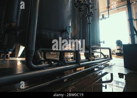 Stainless steel brewing equipment, large reservoirs or tanks and pipes in modern beer factory. Brewery production, industrial interior. Stock Photo