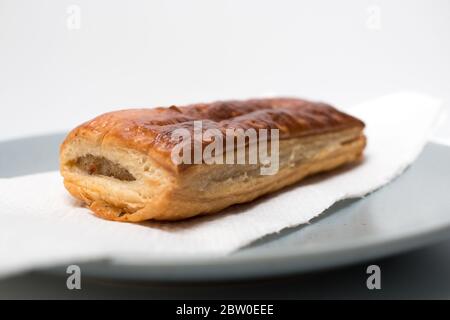 A sausage roll just out of the oven on a plate from the front side on a white background. Saucijzenbroodje. Stock Photo