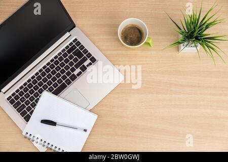 Top view of workspace. Table desk with laptop, coffee, notepad, pen and plant with empty space background for design. Flat lay view of light brown woo Stock Photo