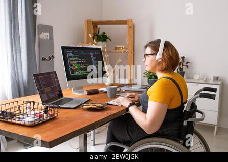 Smart disabled coder sitting in wheelchair and using computers while working from home Stock Photo