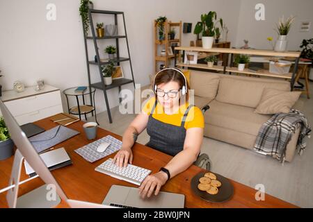 Concentrated young female programmer sitting in wheelchair and using computers while working at home Stock Photo