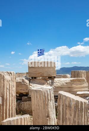 Athens Acropolis, Greece. Greek flag waving on pole, ancient column remains against blue sky background, spring sunny day. Stock Photo