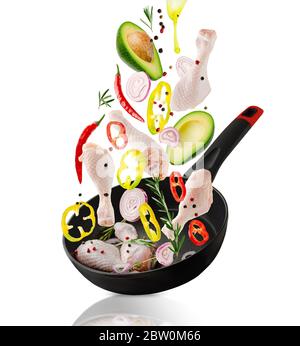 Raw chicken drumsticks and veggies ingredients falling into the frying pan. Isolated on white. Healthy eating Stock Photo
