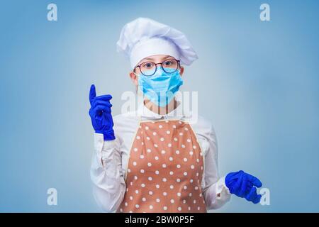 Girl cook wears a protective medical mask and rubber gloves. Virus protection and kitchen safety, pandemic concept. Isolated on blue background. Hight quality photo Stock Photo
