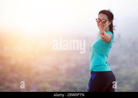 Sportswoman reaches a mountain top and raises arms celebrating the achievement and success of her physical activity purpose. Stock Photo