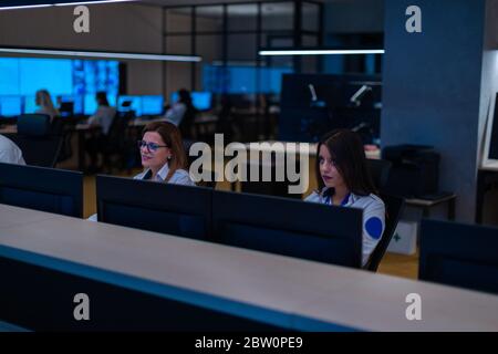 Group of Security data center operators (administrators) working in a group at a CCTV monitoring room while looking at multiple monitors ( computer sc Stock Photo