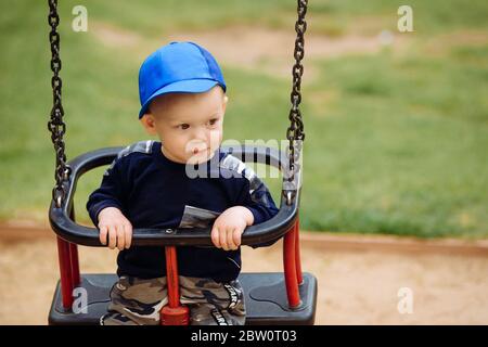 Funny and handsome boy rejoices, rides on a children's swing, plays on the playground, 1-2 years Stock Photo