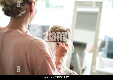 Rear view of hairstylist making bridal hairstyle. Hairdresser attaching