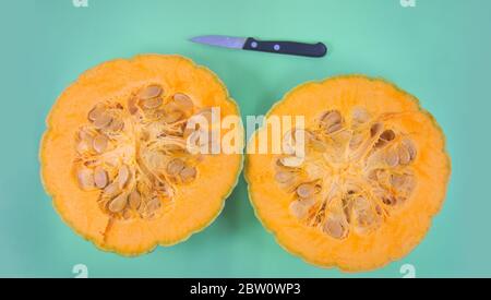 Flat lay of a pumpkin cut in two in half with its seeds and the knife that has been used to make the cut Stock Photo