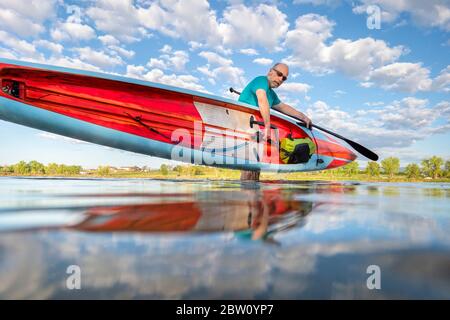 senior male paddler is finishing his morning paddling workout on a racing stand up paddleboard, solo paddling as fitness and training with social dist Stock Photo