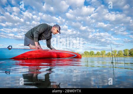 senior male paddler preparing his stand up paddleboard for morning paddling workout, solo paddling as fitness and training with social distancing Stock Photo