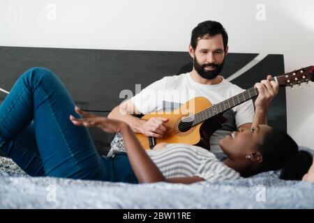Man Playing Guitar And Woman Singing Song In Bedroom Stock Photo