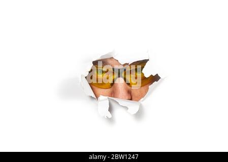 Man in shooting glasses peeping through hole on paper. Male in ellow glasses looking through hole. Isolated on white background. Spy concept Stock Photo