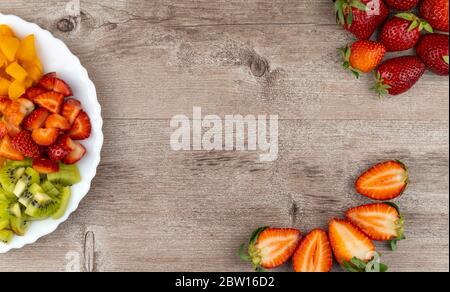 fruit salad and fresh strawberries on wooden table. healthy and dietary breakfast, food preparation concept. Stock Photo