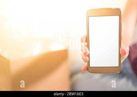Stock photo of a hand holding a cellphone with an empty white screen. Copy space. Empty cellphone near a shopping box. Stock Photo