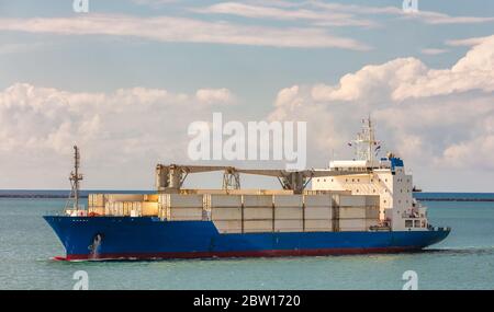 Cargo ship in Panama Canal. Various containers and cranes on deck. Shipping industry concept. Clouds and blue sky as a background Stock Photo